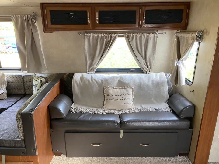 Inside an RV rental, a cozy living area features a dark sofa, light blanket, pillow, curtains, & wood cabinets.. Forest River Salem 2015