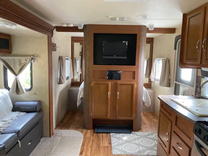 Cozy RV rental interior featuring a living area with a sofa, a central media console, a bedroom beyond, and a full kitchen.. Forest River Salem 2015