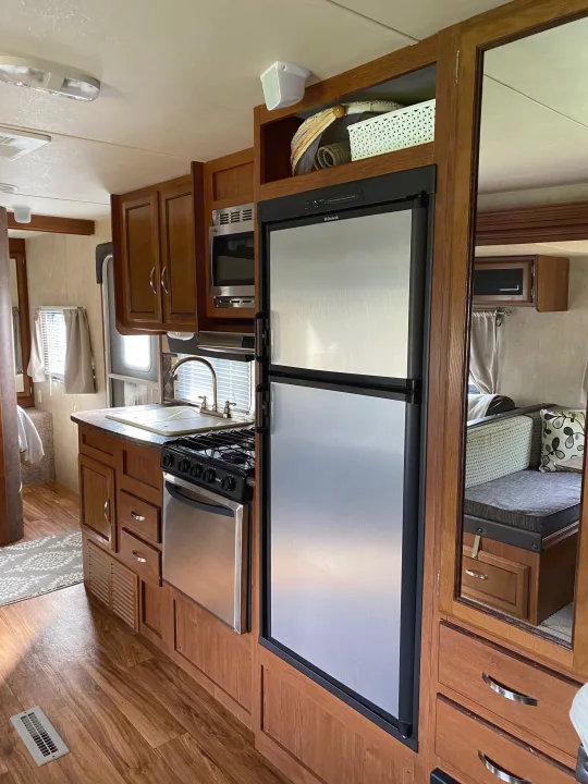 Inside this RV rental: a kitchen with stainless steel fridge, microwave, sink, stove, wood cabinets, and dinette visible.. Forest River Salem 2015