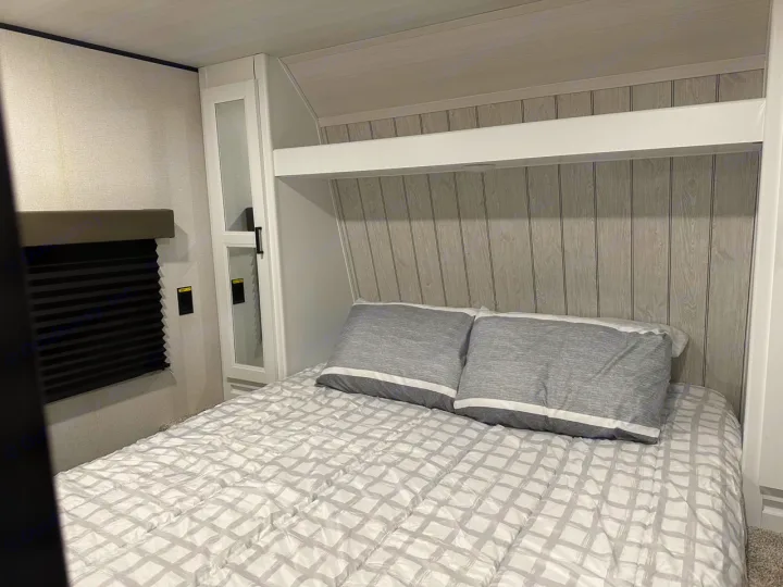 Cozy RV rental bedroom featuring a full bed, built-in storage, and window with blinds. Ideal for travel.. Keystone RV Hideout 2022