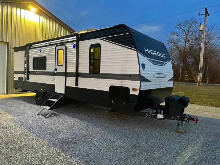 Sleek black & white Hideout travel trailer, ideal for rv rental, parked on gravel. Perfect for camping trips.. Keystone RV Hideout 2022