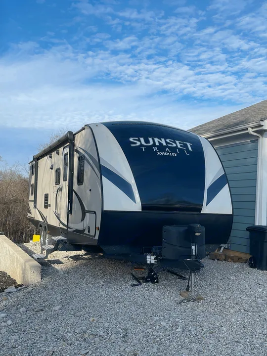 A modern 'Sunset Trail Super Lite' travel trailer (RV rental) parked on gravel, with a clear blue sky overhead.. Crossroads RV Sunset Trail Super Lite 2018