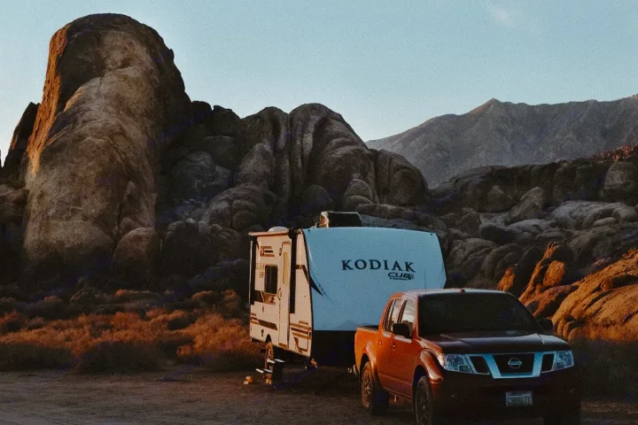 RV rental setup in a rugged desert with a truck, trailer, and massive rock formations at golden hour.. Dutchmen Kodiak Cub 2020
