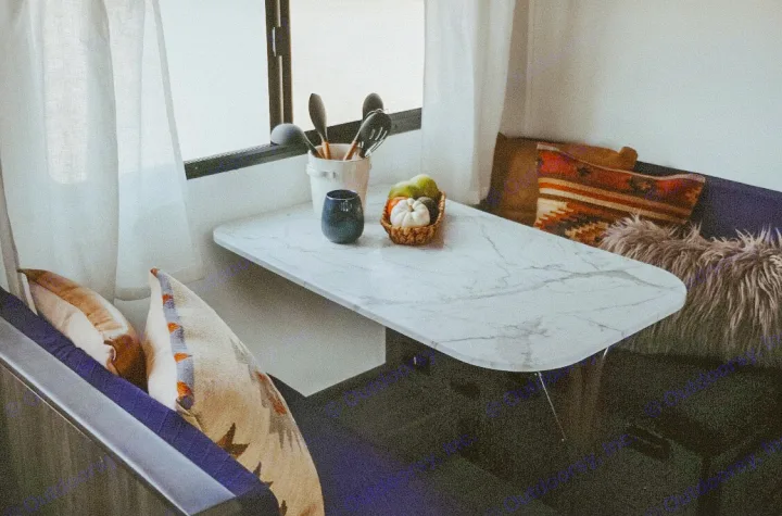 Cozy RV rental dining space: marble table, bench seating with pillows, kitchen tools, and autumnal decor by a window.. Dutchmen Kodiak Cub 2020