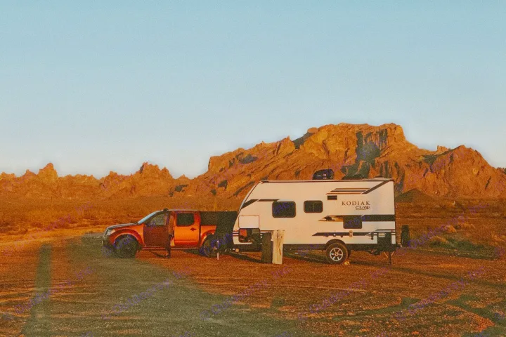 Red truck and an RV rental parked for off-grid camping in a vast desert landscape with golden mountains at dusk.. Dutchmen Kodiak Cub 2020