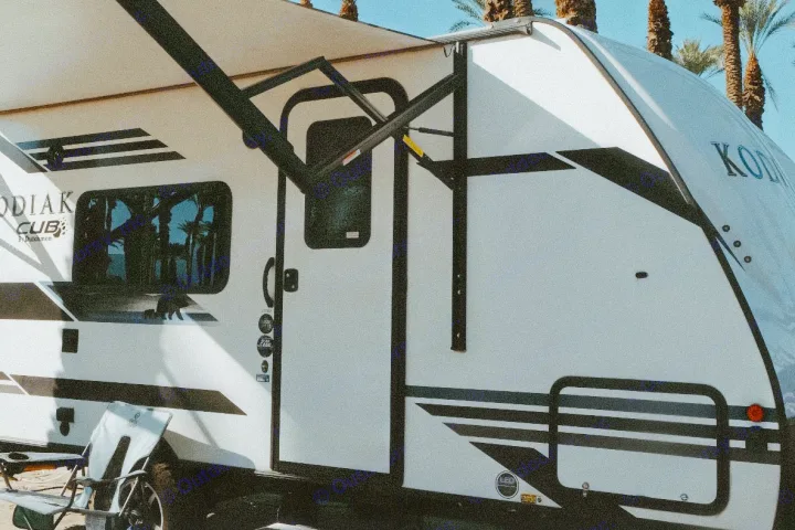White Kodiak Cub RV rental with extended awning, reflecting palm trees. Ready for your camping adventure!. Dutchmen Kodiak Cub 2020