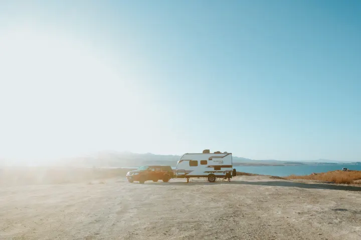 Bright sun over a red truck towing an RV rental parked lakeside. Enjoy vast desert views and outdoor camping.. Dutchmen Kodiak Cub 2020