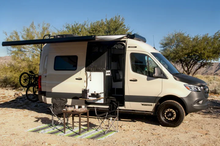 Beige camper van RV rental with outdoor kitchen, dining setup & bike rack, perfect for desert adventures.. Winnebago Revel 2023