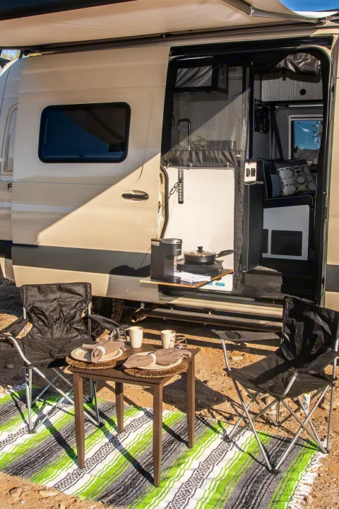 RV rental showing outdoor kitchen with coffee maker, dining table, chairs, and a colorful rug.. Winnebago Revel 2023