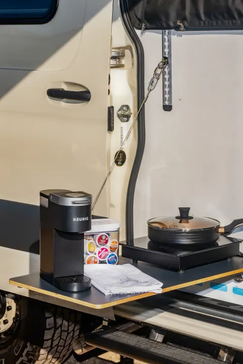 RV rental outdoor kitchen featuring a Keurig coffee maker, cooktop, and pan. Perfect for adventurers on the go.. Winnebago Revel 2023