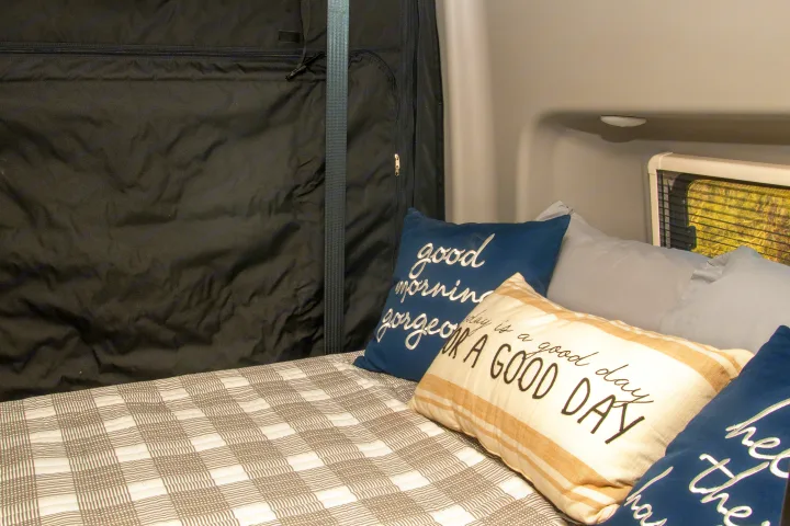 Cozy RV rental interior: a comfy bed with plaid quilt, decorative pillows, and window.. Winnebago Revel 2023