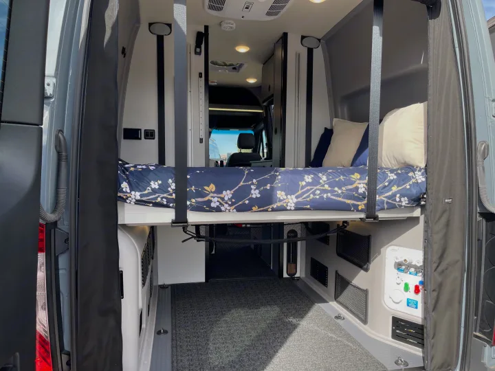 Inside an RV rental: A clever raised bed over a large cargo space, equipped with controls, perfect for van life adventures.. Winnebago Revel 2023