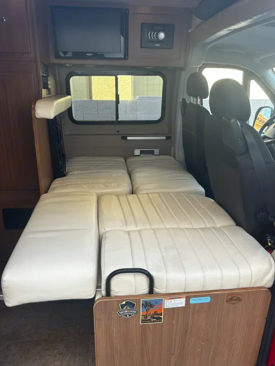 Spacious RV rental interior featuring cream cushions, a convertible bed, overhead TV, stereo, and front cabin view.. Winnebago Travato 2015