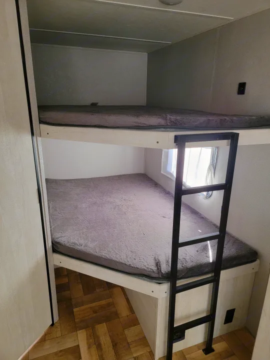 RV rental interior: two bunk beds with grey bedding, a black metal ladder for the top bunk, and a skylight above.. Forest River Shasta 2022
