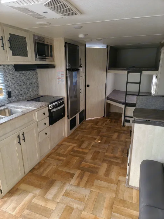 Spacious RV rental interior featuring a modern kitchen with microwave and stove, plus comfortable bunk beds and wood-look flooring.. Forest River Shasta 2022