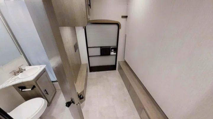 This RV rental shows a compact bathroom, functional hallway with built-in storage/seating, and rear door for versatile living.. Coachmen Freelander 2023