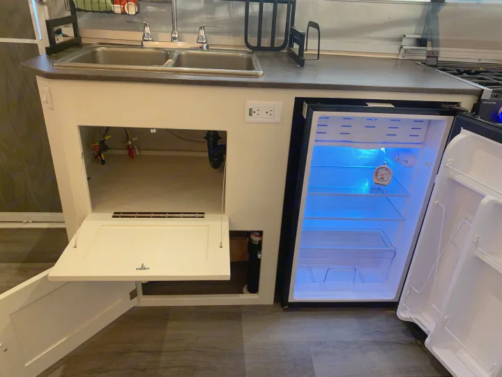 RV rental kitchen with double sink, open mini-fridge glowing blue, and under-sink cabinet open for plumbing access.. Forest River Flagstaff 2007