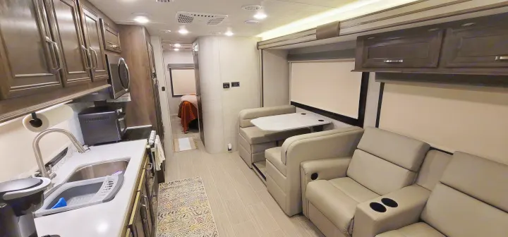 Spacious RV rental interior with kitchen, dining booth, and recliners, leading to a bedroom. Perfect for your next adventure.. Entegra Esteem 29v 2022