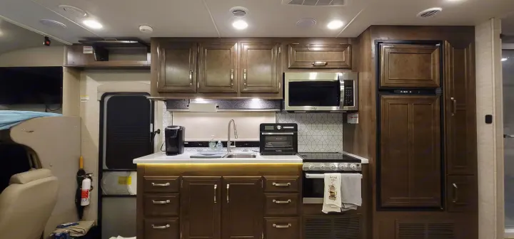 Well-appointed RV rental kitchen features microwave, stove, sink, and fridge, plus a cozy living space.. Entegra Esteem 29v 2022