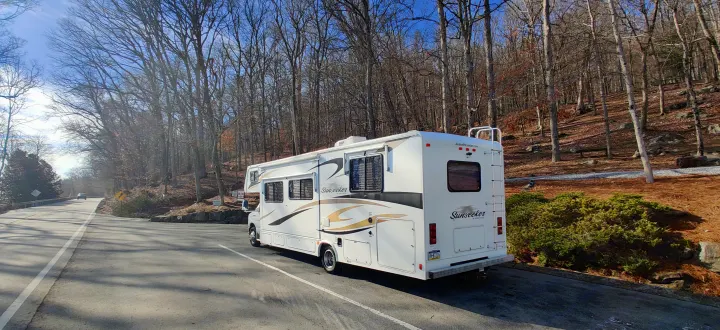 White Forest River Sunseeker RV rental parked roadside in a sunny, bare-tree forest, perfect for outdoor travel.. Forest River Sunseeker 2012