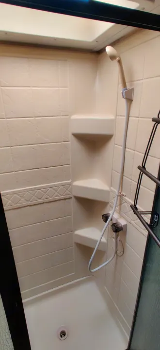 Compact shower in an RV rental with textured walls, corner shelves, and a handheld sprayer for convenience.. Forest River Sunseeker 2012