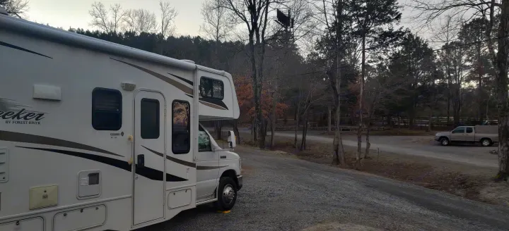 A white Class C RV rental is parked on a gravel road in a rustic campground setting, surrounded by trees.. Forest River Sunseeker 2012