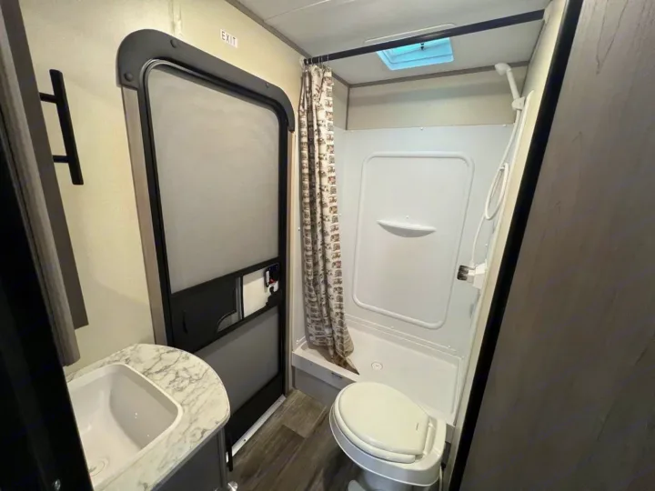 Inside a modern RV rental: a compact bathroom featuring a full shower, toilet, sink, and skylight overhead.. Dutchmen Coleman Lantern LT 2022