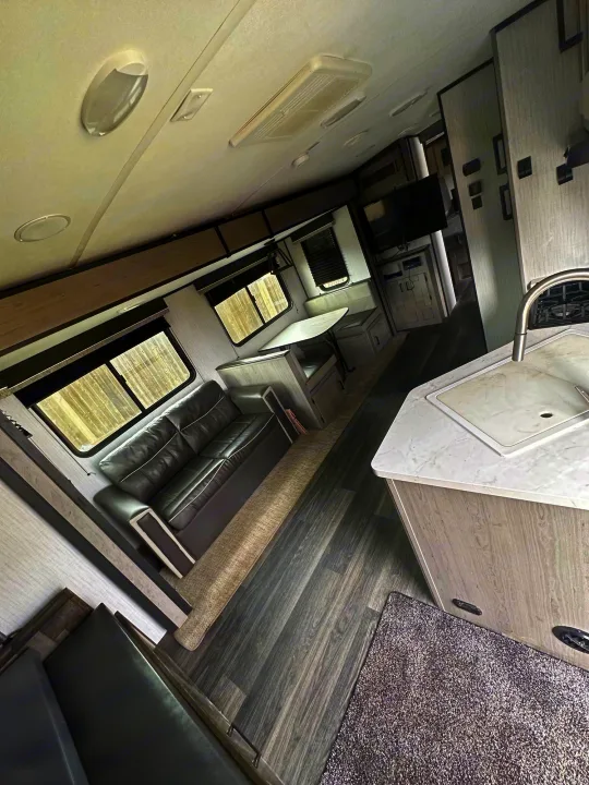 This RV rental's bright interior features a modern kitchen, comfortable sofa, and dining area, all with dark wood-look flooring.. Heartland Other 2021