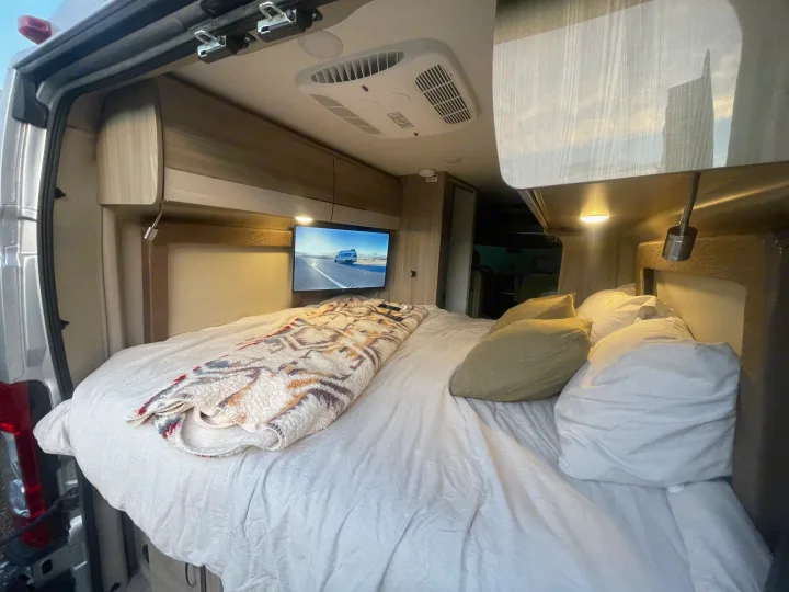 Relax in this comfy RV rental! Interior view of a van's bed, TV, and overhead AC unit with open rear doors.. Thor Sequence 2021
