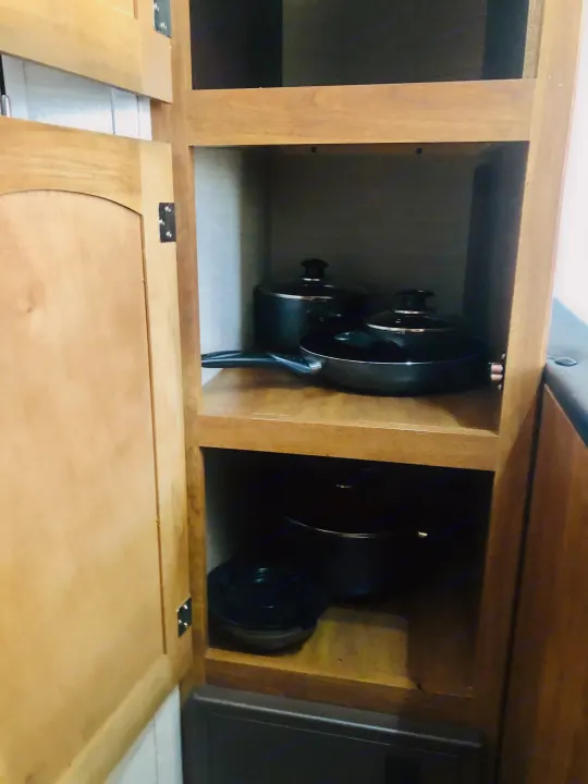 Inside an RV rental kitchen cabinet: light wood shelving storing black pots and pans. Organized cooking essentials.. Keystone RV Springdale Eco-Lite 2016
