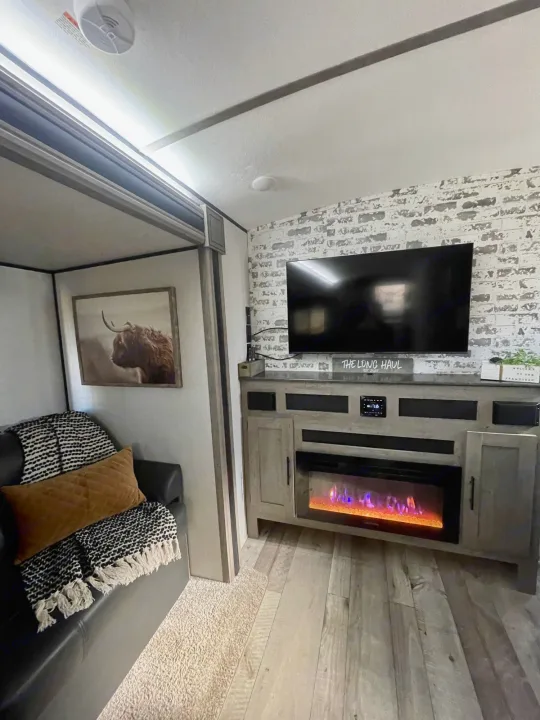 Cozy RV rental living space featuring a TV, electric fireplace, and charming Highland cow artwork for ultimate comfort.. Keystone RV Springdale 2021