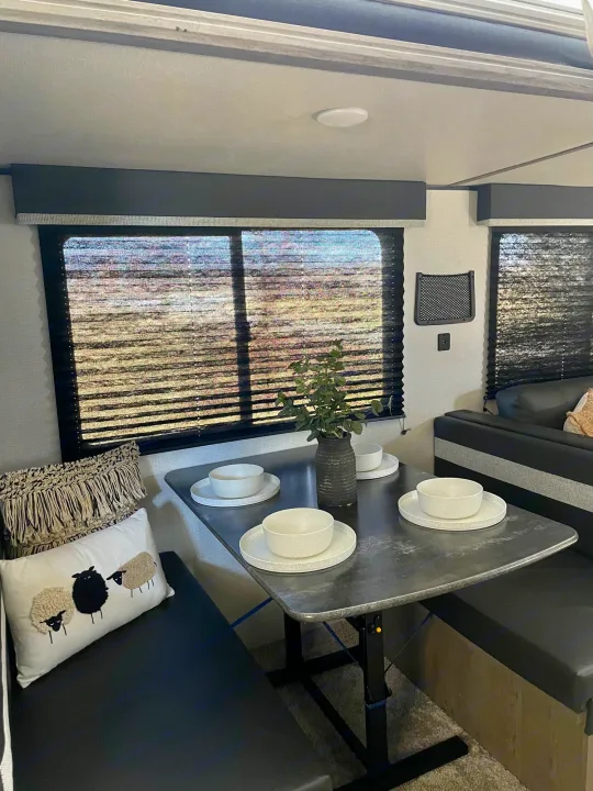RV rental interior: Cozy dining area with a table set for four, comfortable benches, and shaded windows.. Keystone RV Springdale 2021