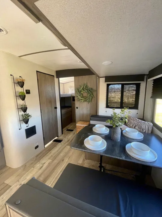 Inside a modern RV rental: dining table set for 4, with bunks and decor visible through the doorway. Light, functional space.. Keystone RV Springdale 2021