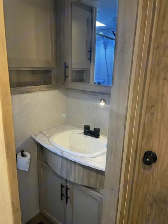Clean RV rental bathroom showcasing a white sink, black faucet, wood-look vanity, cabinet storage, and toilet paper.. Forest River Cherokee Arctic Wolf 2022