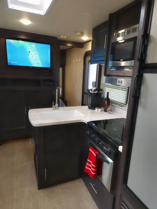 Spacious rv rental kitchen with modern amenities like a Keurig, stove, microwave, and TV showing a Florida map.. Dutchmen Kodiak Ultra Lite 2019