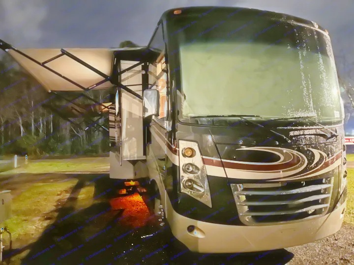 RV rental parked at a dark, rainy campsite. Awning and slide-outs extended, with water drops on the windshield.. Thor Challenger 2015
