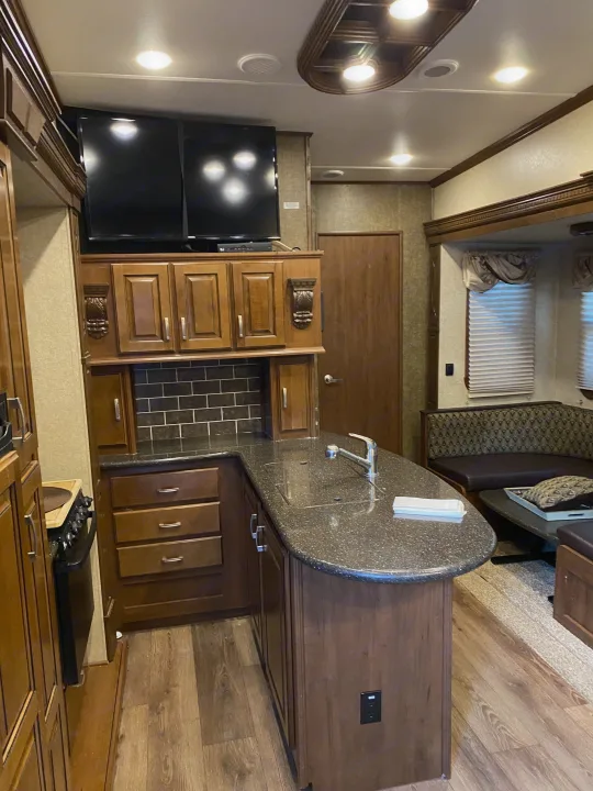 Spacious RV rental interior featuring a modern kitchen island, dining booth, & living area with wood finishes.. Heartland RVs Gateway 2015