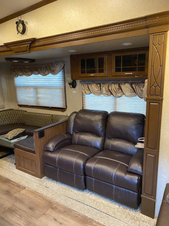 Spacious RV rental living area featuring a brown leather two-seat recliner, patterned dinette, and rich wood cabinetry.. Heartland RVs Gateway 2015