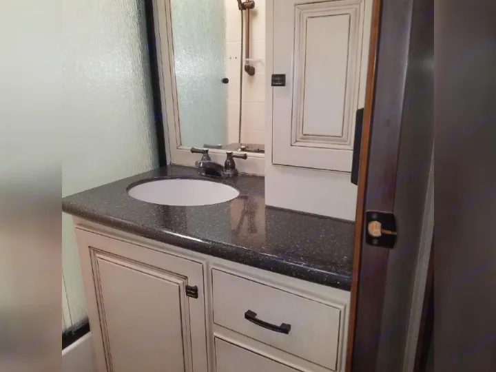 This RV rental bathroom boasts a sleek dark countertop vanity with white sink, light cabinets, and frosted glass shower.. Heartland RVs Gateway 2015