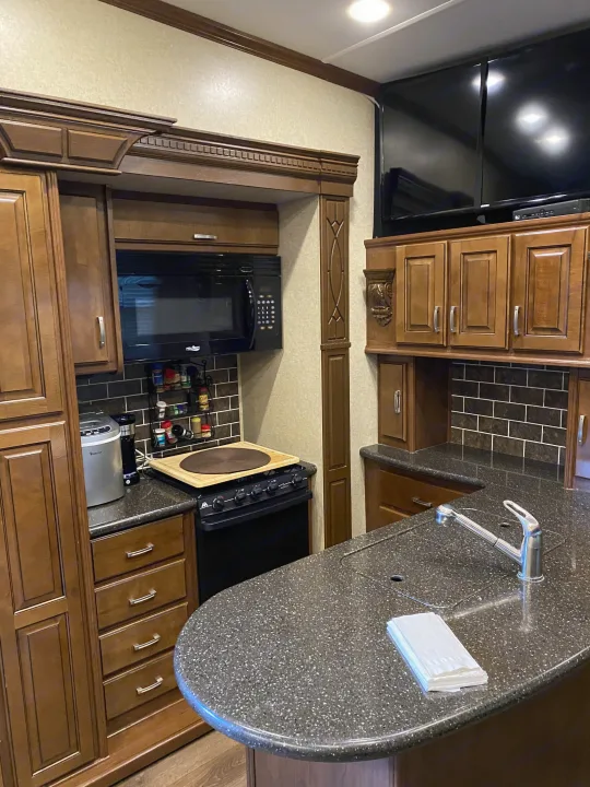 Spacious RV rental kitchen with modern amenities: counter, sink, stove, microwave, and TV, perfect for travel.. Heartland RVs Gateway 2015