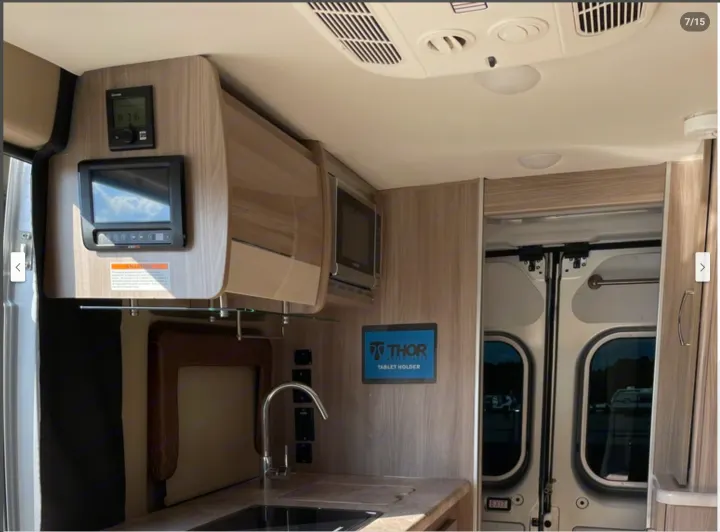 Compact RV rental interior featuring a kitchen with sink, microwave, overhead storage, and mounted control panels.. Thor Motor Coach Scope 2022