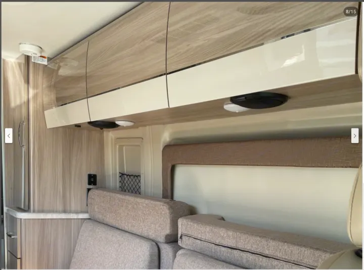 Modern RV rental interior with light wood overhead cabinets, white doors, under-cabinet lights, and cozy gray cushions.. Thor Motor Coach Scope 2022