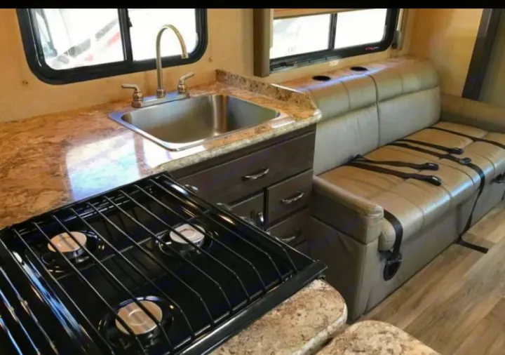 This RV rental features a compact kitchen with a sink, 3-burner stove, and a dinette with seatbelts, ready for travel.. Thor Four Winds 2019