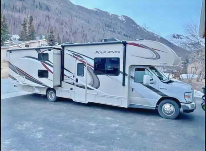 Four Winds RV rental with slide-outs, perfect for mountain adventures. This motorhome is parked in a scenic setting.. Thor Four Winds 2019
