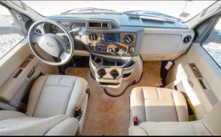 Interior of an RV rental: driver's view of the cabin, dashboard with screen, steering wheel, and two front seats.. Thor Four Winds 2019