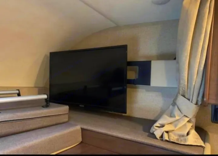 Spacious RV rental interior with a wall-mounted TV over carpeted steps leading to an elevated bunk. A curtain is on right.. Thor Four Winds 2019
