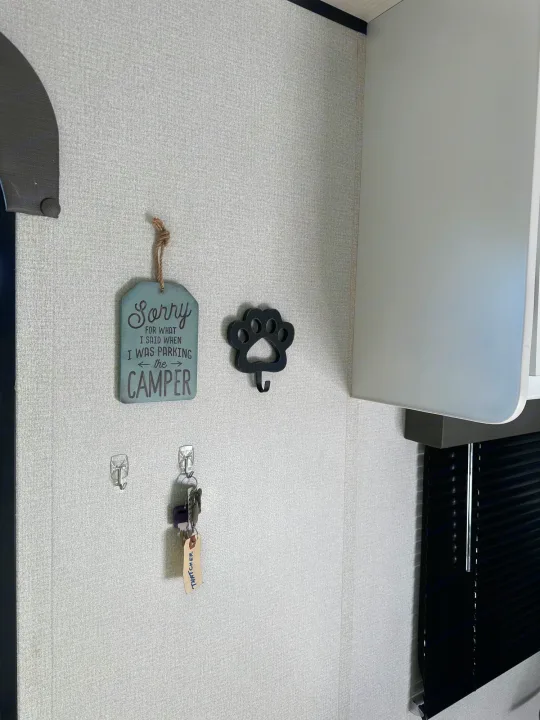 An rv rental interior showing a "Sorry for parking the camper" sign, paw hook, & keys on wall hooks.. Keystone RV Hideout 2022