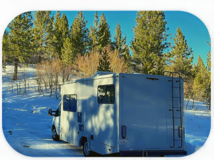 Snowy adventure awaits! This RV rental is parked in a winter wonderland among tall pine trees, perfect for a cozy trip.. Coachmen Crosstrail 20XG 2022