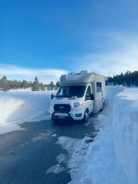 White rv rental, a Ford Transit camper, is parked between towering snow walls on a sunny winter day.. Coachmen Crosstrail 20XG 2022