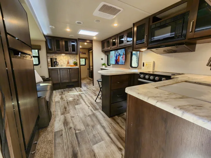 This bright RV rental interior showcases a well-equipped kitchen, comfortable seating, and stylish wood-look flooring.. Grand Design Transend Xplor 315BH 2023
